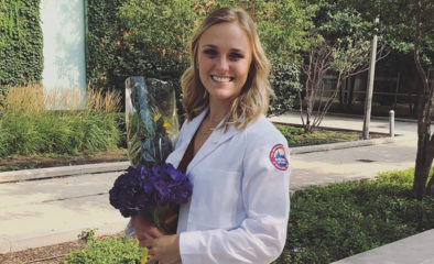 Savannah Soppet wearing a white medical coat and holding flowers