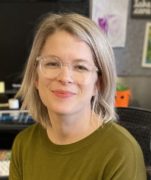 headshot of woman with short blond hair, glasses, and a green shirt.