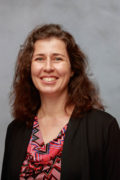 Smiling white woman with long, dark hair wearing a red print blouse and black sweater