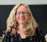 white woman smiling with long blonde hair wearing glasses and a black blouse