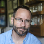 Photograph of Cameron Slayden with a blue shirt and a short beard. 