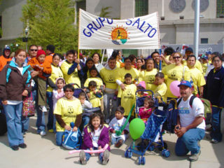 A group of families outside at a walk holding a Grupo SALTO banner