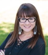 Hailee Yoshizaki-Gibbons, a White/Asian woman, wearing square black rimmed glasses and smiling.
