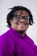 Smiling African-American cis-male genderqueer person, with locs, purple shirt, and glasses