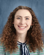 Yearbook headshot of Sarah Chew a white woman with curly red/brown hair smiling at the camera wearing a green and blue striped shirt. Background is blue gradient.