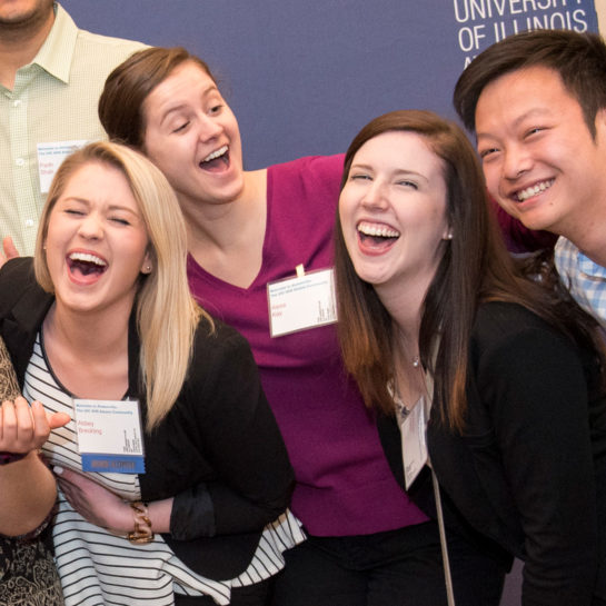 A group of three female students and one male laughing in front of a UIC banner