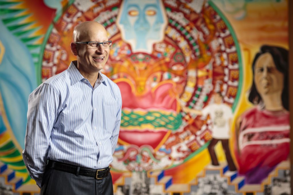 Carlos Crespo stands in front of a colorful wall mural