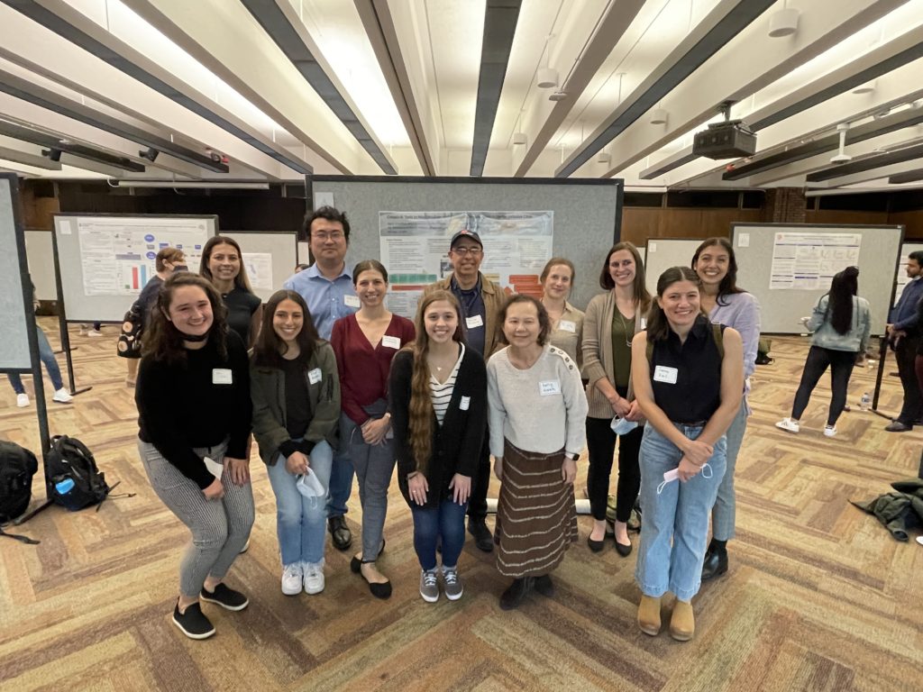 DHD students, faculty and staff stand in a group in front of a research poster