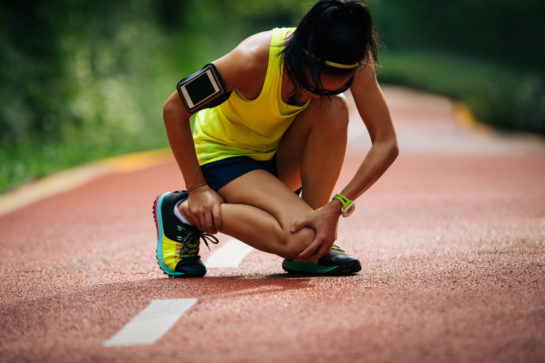 woman crouches on a track holding her knee
