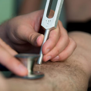 Closeup of physical therapist's hands using stethoscope and tuning fork on patient's leg
