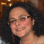 Head of smiling woman with curly hair and glasses.