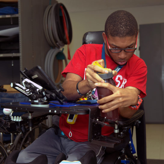 An ATU wheelchair-bound client tests a new assistive device installed on hiw sheelchair to hold items such as water bottles
