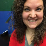 girl smiling, wearing a red blazer jacket with grey shirt underneath